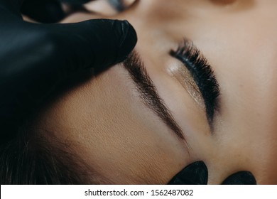 A Microblading Master In Black Rubber Gloves Holds A Close-up Of A Girl’s Client’s Finished Eyebrow.