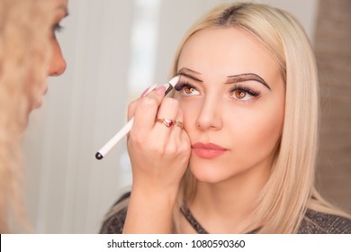 Microblading, micropigmentation eyebrows work flow in a beauty salon. Woman having her eye brows drawn and tinted with black pencil, preparing for semi-permanent makeup for eyebrows. Focus on eyebrow