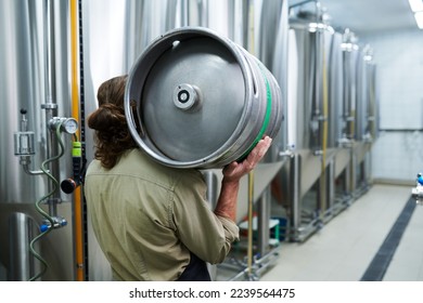 Microbrewery worker carrying beer keg to warehouse, view from back - Powered by Shutterstock