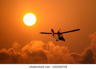 A microlight aircraft with two passengers with the sun and cloud