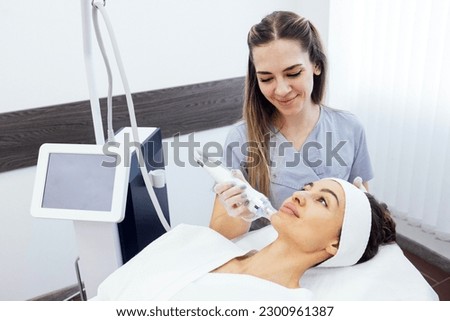 Microneedle RF lifting procedure. Hardware cosmetology. Beautician conducts a facial rejuvenation procedure for a brunette woman