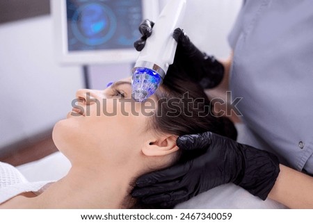 Microneedle RF lifting procedure. Hardware cosmetology. Beautician conducts a facial rejuvenation procedure for a brunette woman