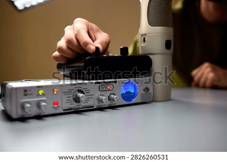 Microphone and audio interface adjusting settings on an audio interface, in indoor likely a studio or home office environment, with microphone, audio interface, with green, black accents.