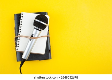 Microphone and empty open note book on yellow paper background. Copy space for your text. Blog, potcast concept