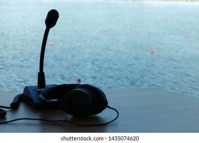 Microphone And Headphones For Sports Commentator On The Background Of Water And Buoys.