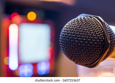 Microphone In A Karaoke Bar. Close Up Shot Of A Black Mic With Karaoke Screen Monitor In The Background. 