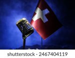 Microphone on a background of a blurry flag of Switzerland close-up. dark table decoration. Selective focus