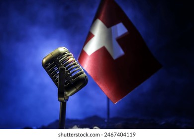 Microphone on a background of a blurry flag of Switzerland close-up. dark table decoration. Selective focus