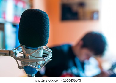 Microphone On Focus, Playing Young Guitarist On Background In A Small Music Studio, Shallow Depth Of Field.