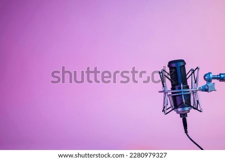 a microphone on a gradient pink and purple background under the neon light with copy space for podcasting, singing, and recording background.