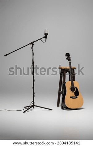 Microphone on metal stand and acoustic guitar near wooden brown chair on grey background