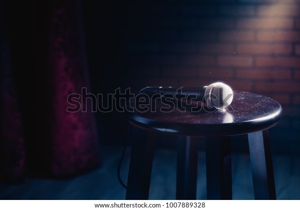 microphone on a wooden stool on a\
stand up comedy stage with reflectors ray, high contrast\
image