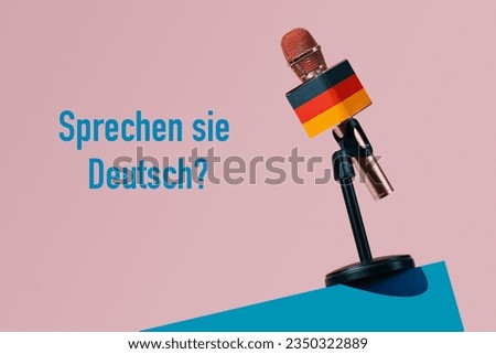 a microphone patterned with the german flag, in a black stand on a blue table, and the question do you speak german written in german on a pink background