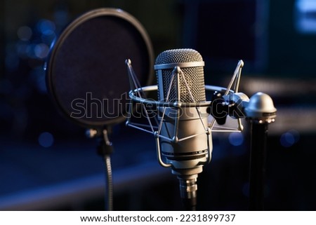 Microphone with a pop shield closeup on the background of a professional recording studio. Microphone stand with a condenser for records vocals, speakers and sound of musical instrument. 