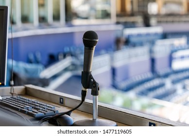 Microphone Resting In Holder On Desk Of Announcers Booth For Baseball Stadium.