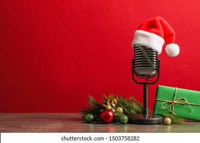 Microphone with Santa hat and decorations on grey table against red background, space for text. Christmas music