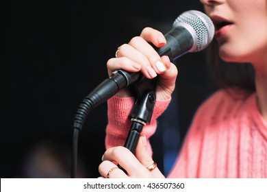 Microphone and unrecognizable female singer close up. Cropped image of female singer in pink dress , singing into a microphone, holding mic with two hands. Copyspace