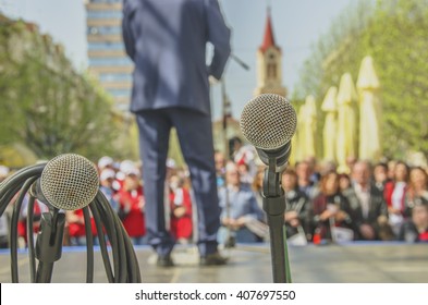 Microphones At Political Rally With Leader And Audience In The Background