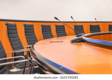 Microphones and round brown table in an empty conference room. Beginning of session meeting with black chair