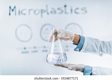 Microplastic pollution concept. Scientist holding a flask with a water sample full of tiny plastic particles against a whiteboard with microplastic pollution graph.