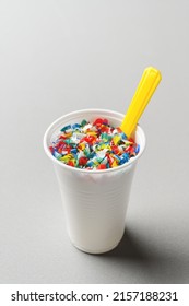 Microplastic in white plastic cup with spoon. Light grey background. Microplastic problem concept. Place for text