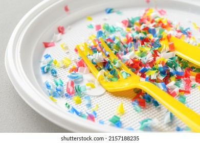 Microplastic in white plastic dish with knife and fork. Light grey background. Microplastic problem concept. Close up