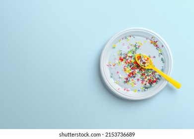 Microplastic in white plastic dish with spoon. Pastel blue background. Microplastic problem concept. Overhead view with place for text