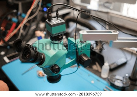 Microscope featuring dual eyepieces and an adjustable arm placed on a blue work surface, surrounded by laboratory equipment and tools