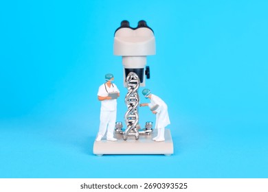Microscope model positioned on a blue background, featuring two miniature scientists analyzing a DNA helix structure on the base, emphasizing genetic research.