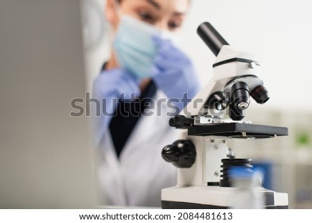 Microscope near blurred scientist in medical mask in laboratory
