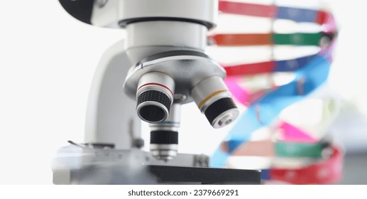 Microscope standing near multicolored model of dna chain in lab. Screening for hereditary genetic diseases concept