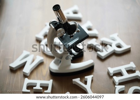 Microscope Surrounded by Scattered Letters on Wooden Table - Science and Education Concept