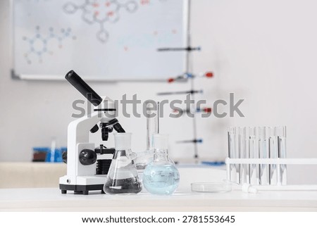 Microscope with test tubes and flasks of water samples on table in research laboratory