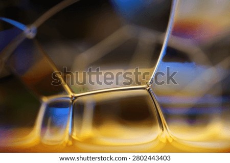 Microscopic fluid framework with glowing gold pillars and prismatic light reflections. Abstract scientific macro photography highlighting an illuminated liquid cell base. Sturdy golden structural vertices and transparent curved walls act as prisms, catching bright amber and cold blue highlights over a dark blurred setting.