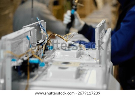 Microwave oven assembly process occurring in factory setting with workers handling components and wiring at a production line