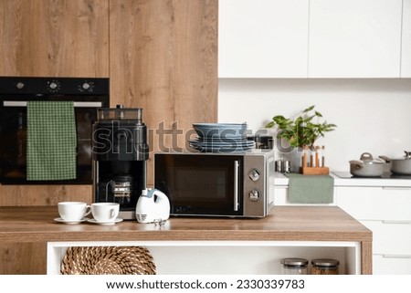 Microwave oven, coffee machine, mixer and set of plates on wooden table in modern kitchen