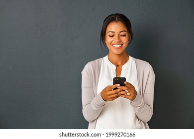 Mid adult african american woman texting message on smart phone isolated on grey background. Smiling indian woman using mobile phone. Happy multiethnic lady messaging on the smartphone with new app.