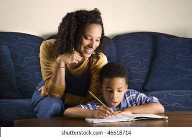 A Mid Adult African American Woman Sits On A Couch And Helps Her Young Some With His Homework. Horizontal Shot.