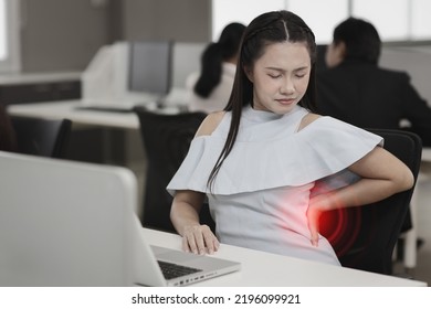 Mid adult asian stressed businesswoman sitting and holding her lower back pain or having problem with part of body backache after working on computer too long time in office. Office syndrome concept - Shutterstock ID 2196099921