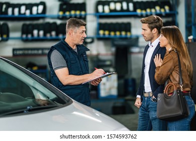 Mid adult auto mechanic talking to a worried couple in a repair workshop.  - Powered by Shutterstock