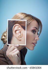 mid adult business woman holding photo of her ear on blue background. Vertical shape, side view, head and shoulders, copy space