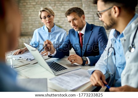 Mid adult businessman and group of doctors working on a computer during a meeting.