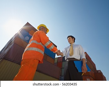 Mid adult businessman holding clipboard and shaking hands to manual worker near cargo containers. Horizontal shape, low angle view. Copy space - Powered by Shutterstock