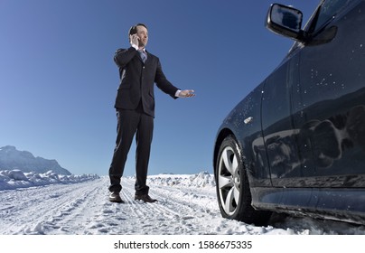 Mid Adult Businessman On Cell Phone Standing Next To Broke Down Car On Snowy Road