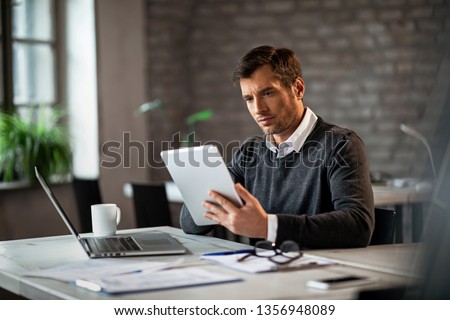 Mid adult businessman working at his desk and surfing the internet on a touchpad. 
