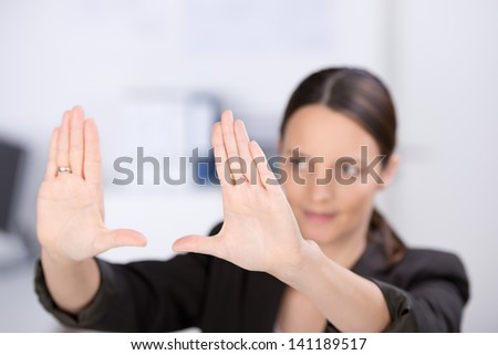 Mid adult businesswoman making hand frame in office, focus hands