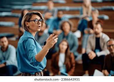 Mid adult businesswoman talking to group of seminar attendees in conference hall.  - Powered by Shutterstock