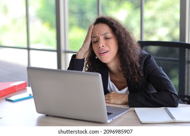 Mid adult businesswoman touching her head on table in office after bad news business failure or get fired and feeling discouraged, distraught and hopeless in modern office. 