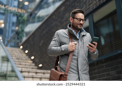 Mid adult Caucasian man in smart casual work attire uses his smartphone, managing tasks with ease outside an office building. - Powered by Shutterstock