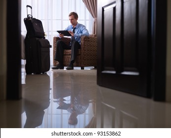 Mid Adult Caucasian Manager Typing On Tablet Pc In Hotel Room During Business Travel. Low Angle View, Full Length